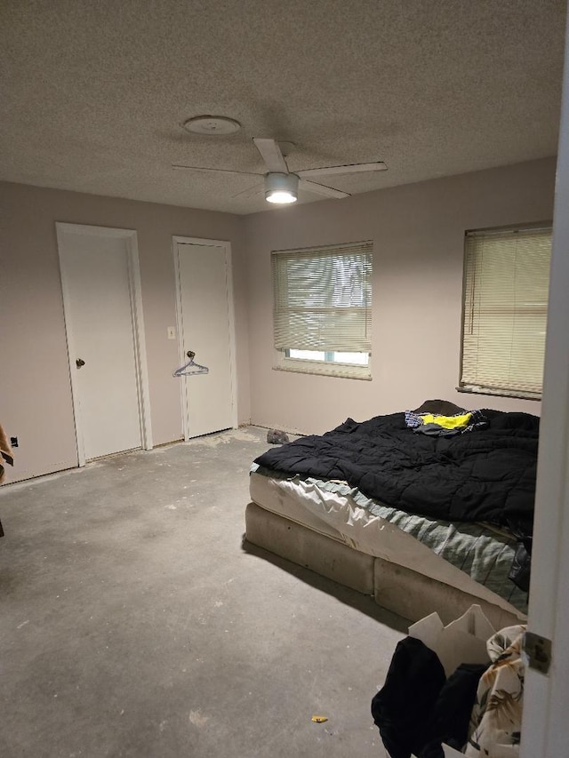 bedroom with ceiling fan, a textured ceiling, two closets, and unfinished concrete floors