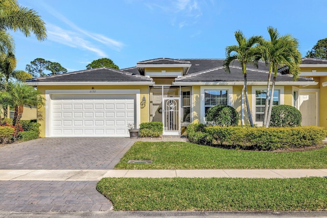 view of front of home with a front yard, stucco siding, a garage, a tiled roof, and decorative driveway