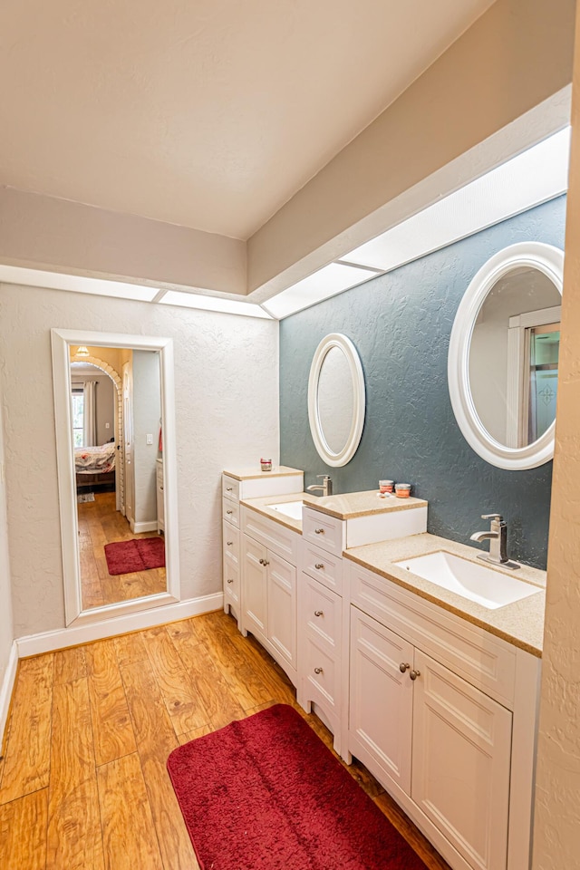 full bathroom with double vanity, wood finished floors, a textured wall, and a sink