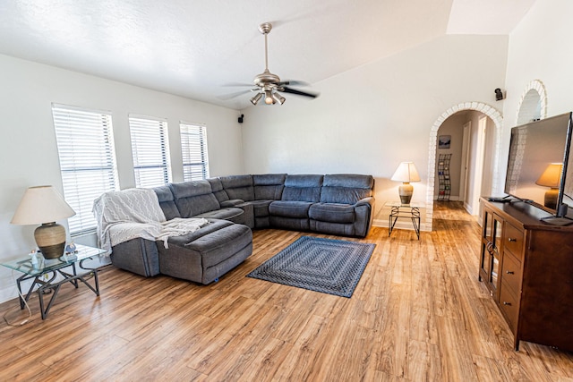 living room featuring a ceiling fan, baseboards, arched walkways, light wood-style floors, and lofted ceiling