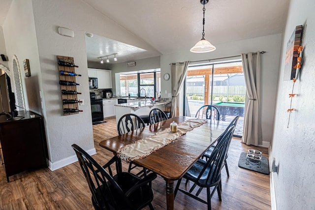 dining room featuring track lighting, a textured ceiling, wood finished floors, baseboards, and a textured wall