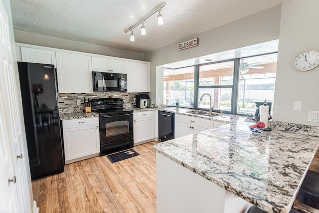 kitchen with light wood finished floors, black appliances, a peninsula, white cabinetry, and a sink