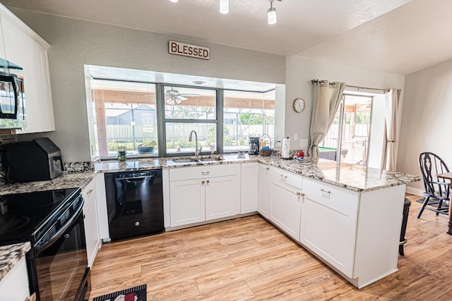 kitchen featuring light wood finished floors, a peninsula, a textured wall, black appliances, and a sink