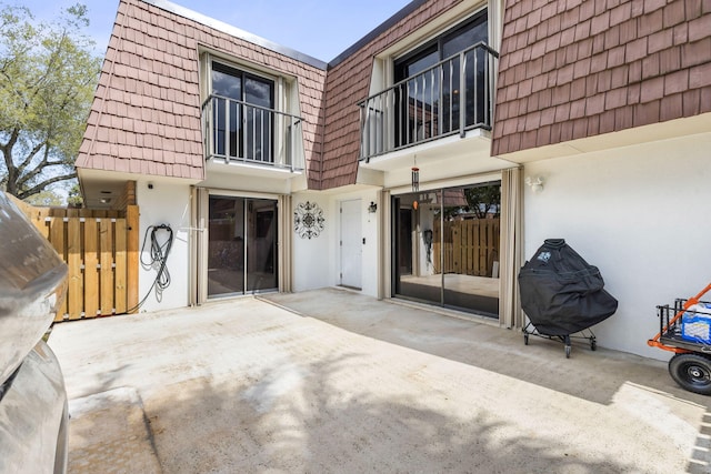 exterior space with a patio area, mansard roof, and stucco siding