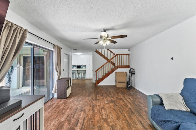 sitting room featuring ceiling fan, a textured ceiling, wood finished floors, baseboards, and stairs