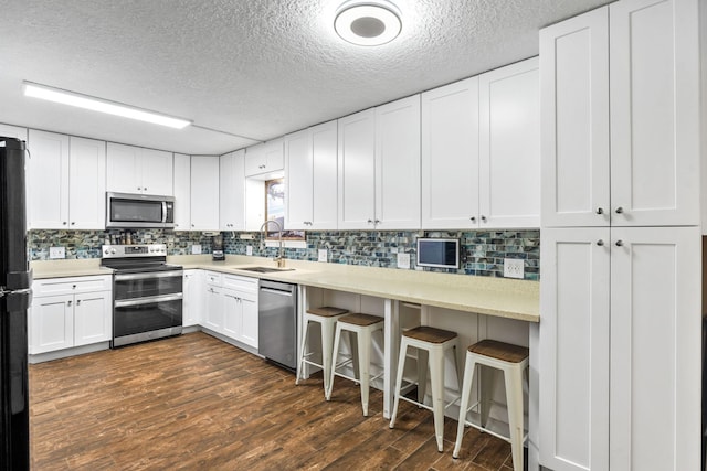 kitchen featuring dark wood-type flooring, a sink, light countertops, appliances with stainless steel finishes, and a kitchen bar