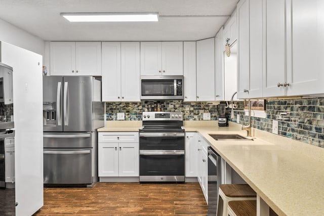 kitchen with dark wood-style flooring, stainless steel appliances, light countertops, backsplash, and white cabinets