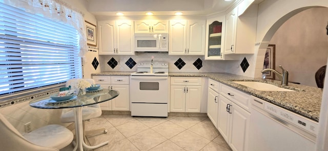 kitchen with white appliances, arched walkways, decorative backsplash, white cabinetry, and a sink