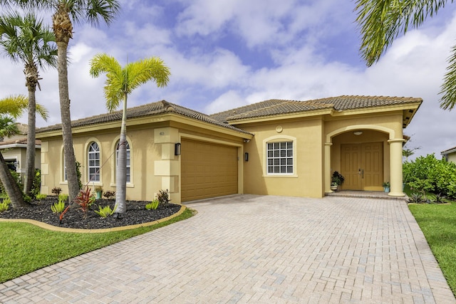 mediterranean / spanish house with stucco siding, an attached garage, a tile roof, and decorative driveway