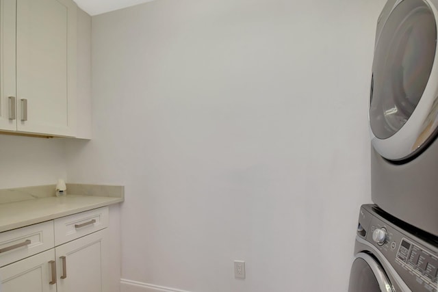 washroom featuring stacked washer and clothes dryer, cabinet space, and baseboards