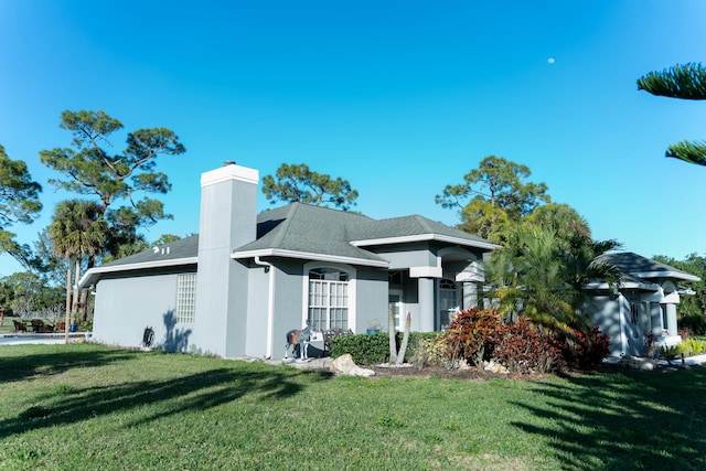 view of front of house with stucco siding, a shingled roof, a chimney, and a front yard