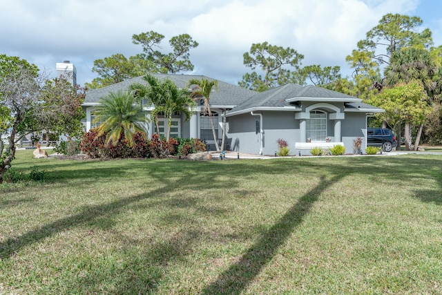 view of front facade with stucco siding, roof with shingles, and a front yard