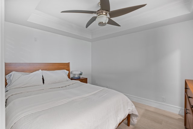 bedroom featuring a ceiling fan, baseboards, light wood-style floors, a raised ceiling, and crown molding