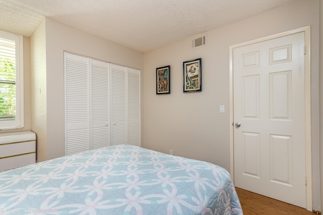 bedroom featuring a closet, light wood-type flooring, a textured ceiling, and visible vents