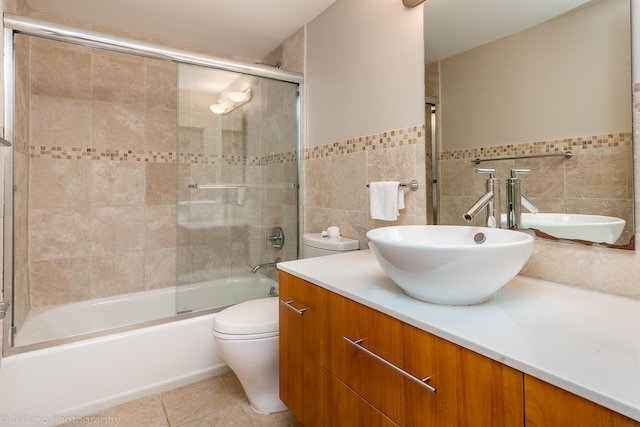 bathroom with vanity, combined bath / shower with glass door, toilet, and tile walls