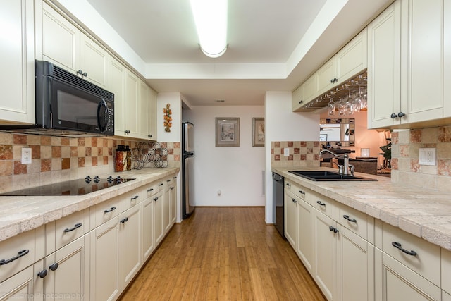 kitchen featuring a sink, decorative backsplash, black appliances, and light wood-type flooring