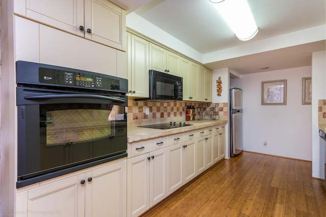kitchen with light countertops, baseboards, light wood-type flooring, backsplash, and black appliances