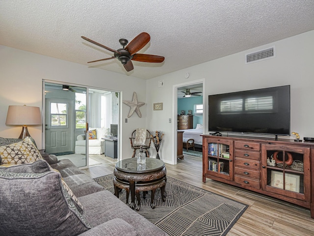 living room featuring light wood-type flooring, a ceiling fan, visible vents, and a textured ceiling