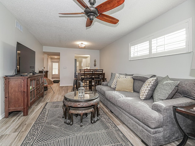 living room with a textured ceiling, visible vents, baseboards, a ceiling fan, and light wood-type flooring