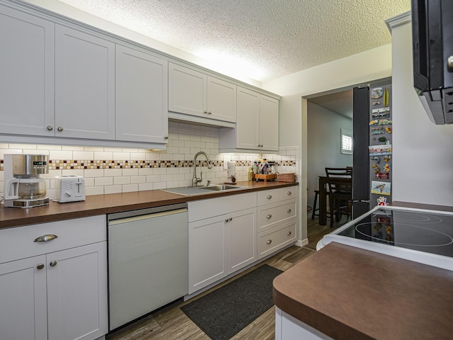 kitchen featuring dark wood-style flooring, tasteful backsplash, freestanding refrigerator, a sink, and dishwasher