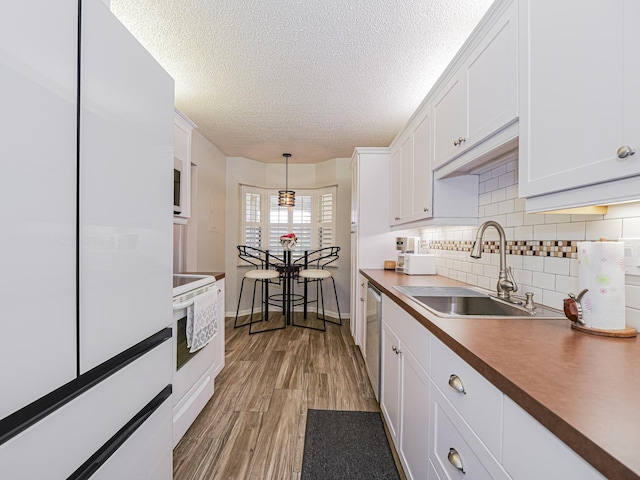 kitchen featuring white appliances, light wood finished floors, white cabinets, a textured ceiling, and a sink