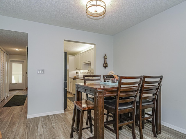 dining area featuring light wood-style flooring, baseboards, and a textured ceiling