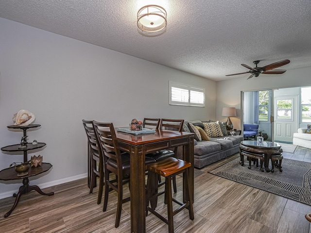 dining space with a textured ceiling, baseboards, and wood finished floors