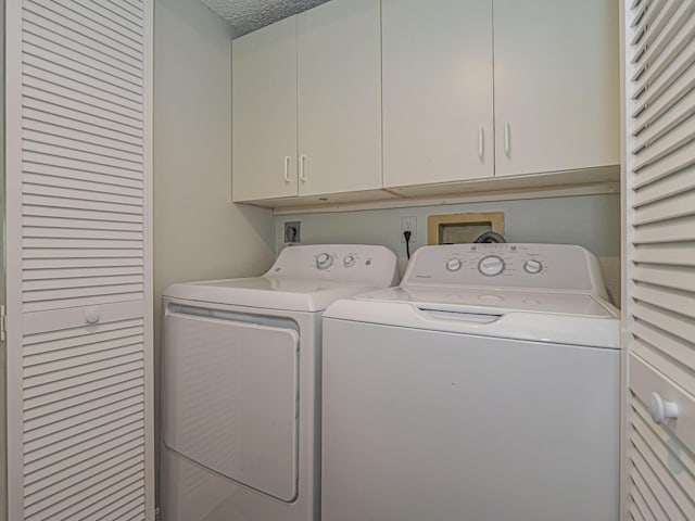 laundry room with a textured ceiling, separate washer and dryer, and cabinet space