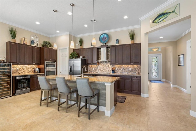 kitchen with a breakfast bar area, appliances with stainless steel finishes, a sink, beverage cooler, and wall chimney exhaust hood