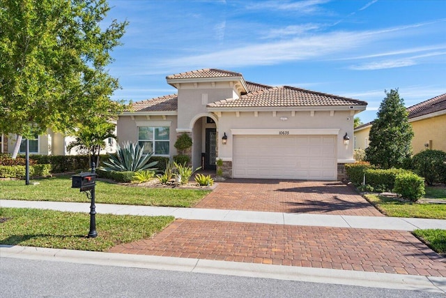 mediterranean / spanish-style house featuring decorative driveway, stucco siding, a front yard, a garage, and a tiled roof