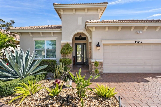 view of exterior entry with a garage, stone siding, decorative driveway, and stucco siding