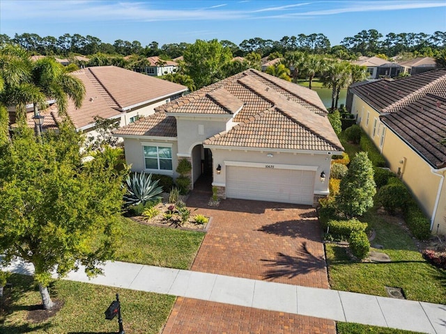 mediterranean / spanish home featuring a garage, a tiled roof, decorative driveway, and stucco siding