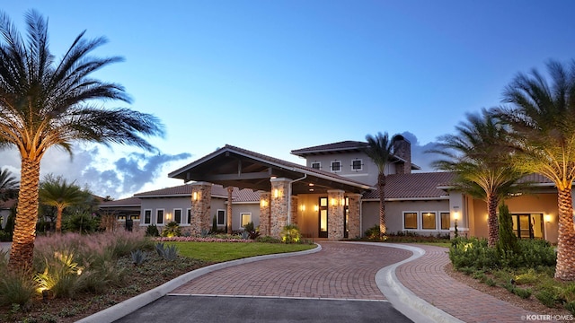 view of front facade with decorative driveway, a tile roof, a chimney, stucco siding, and stone siding