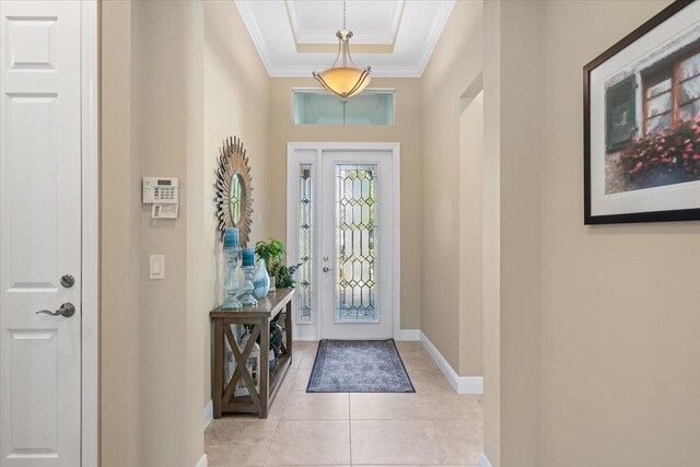 foyer with baseboards, a raised ceiling, crown molding, and light tile patterned flooring