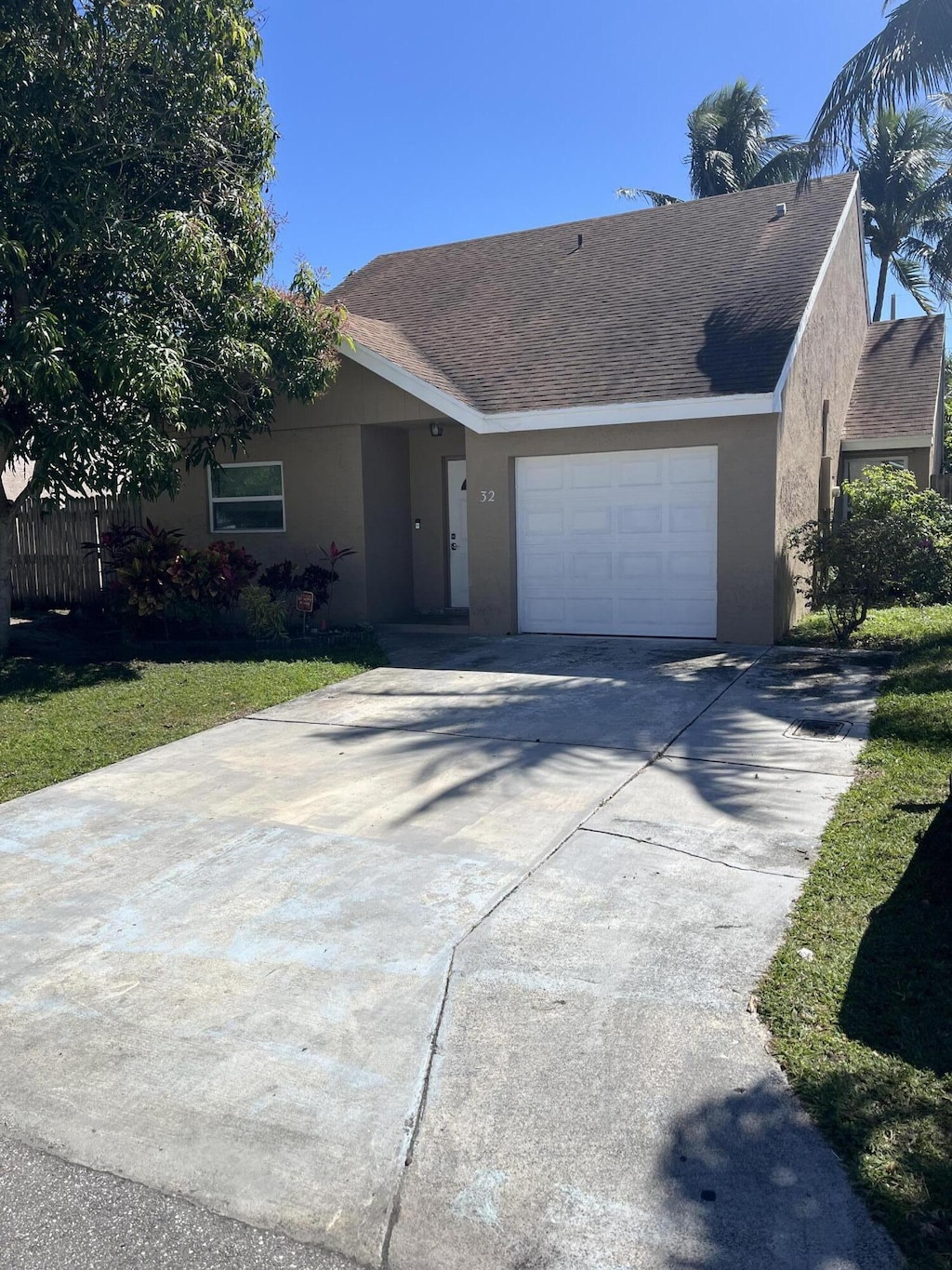 single story home featuring a garage, driveway, roof with shingles, and stucco siding