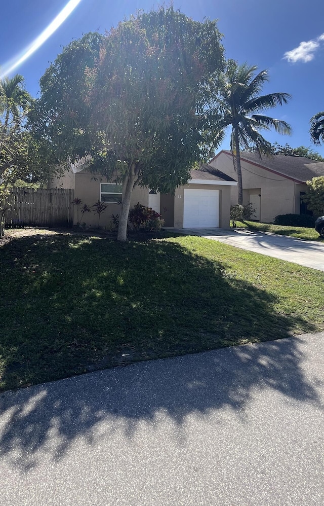 view of front of house with driveway, stucco siding, an attached garage, fence, and a front yard