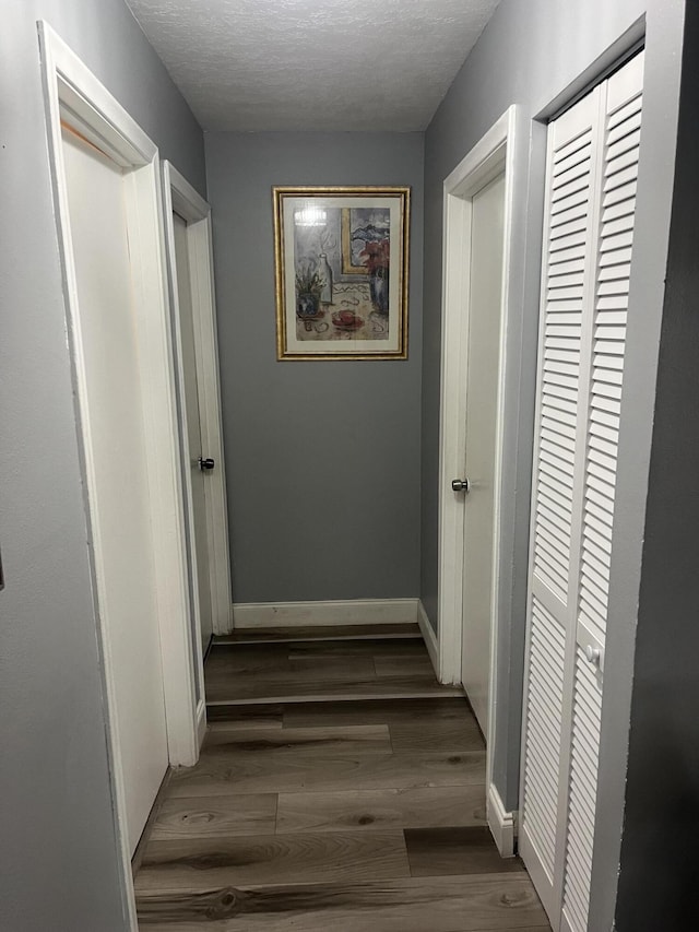 hallway with a textured ceiling, baseboards, and wood finished floors