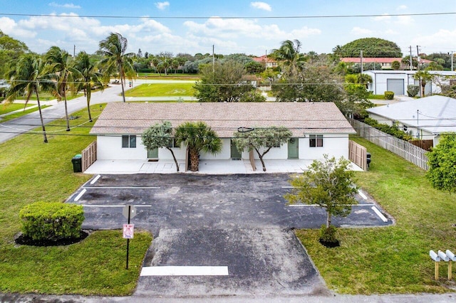 view of front facade with a front yard, uncovered parking, and fence