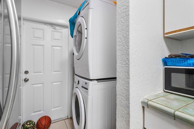 washroom with light tile patterned floors, stacked washing maching and dryer, and a textured wall