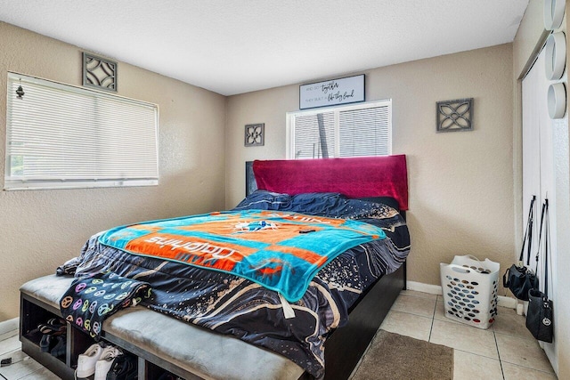 bedroom featuring a textured wall, baseboards, and tile patterned flooring