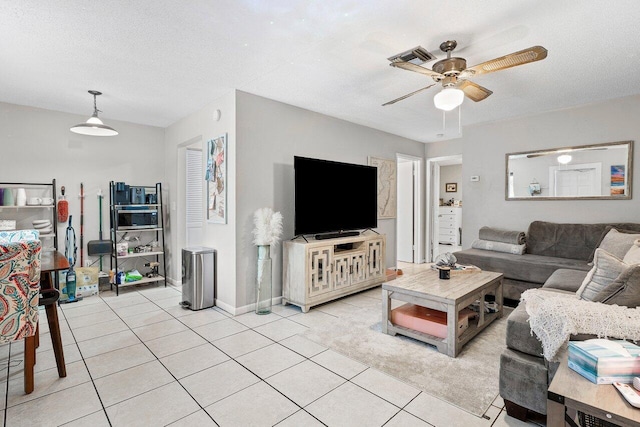 living area featuring light tile patterned floors, visible vents, a textured ceiling, and a ceiling fan