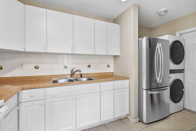 laundry room with light tile patterned floors, laundry area, a sink, stacked washer and clothes dryer, and a textured ceiling