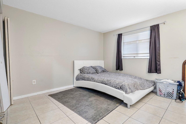 bedroom featuring light tile patterned floors, baseboards, and a textured ceiling