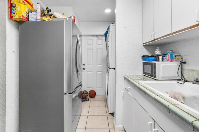 kitchen featuring light tile patterned floors, white microwave, freestanding refrigerator, white cabinetry, and fridge