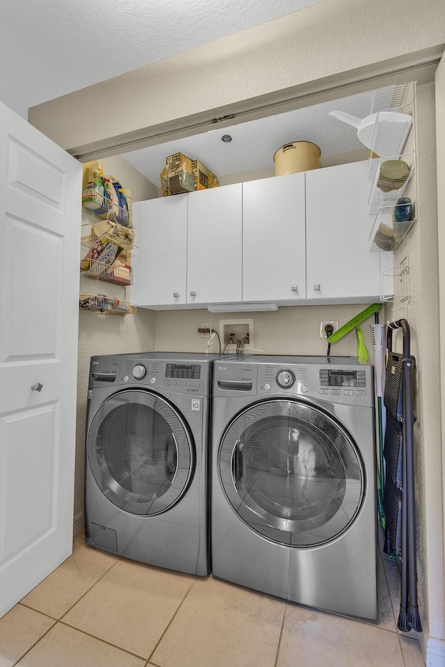 clothes washing area with cabinet space, washing machine and clothes dryer, and light tile patterned floors