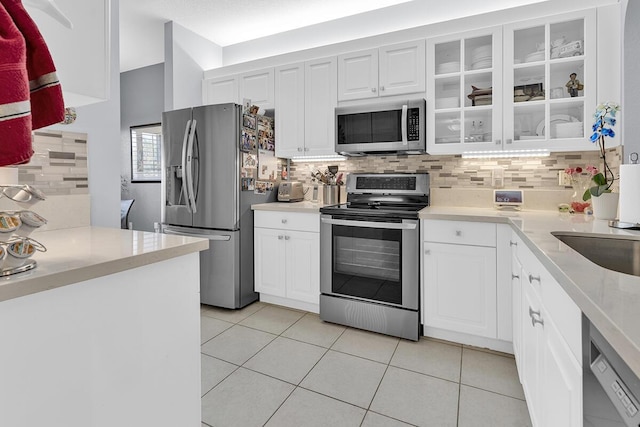 kitchen with light tile patterned floors, stainless steel appliances, tasteful backsplash, and glass insert cabinets