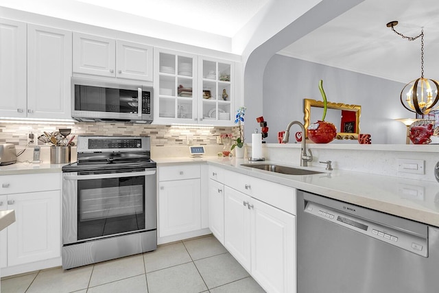 kitchen featuring glass insert cabinets, appliances with stainless steel finishes, a sink, light countertops, and backsplash