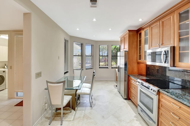 kitchen with stainless steel appliances, visible vents, glass insert cabinets, washer / dryer, and dark stone counters