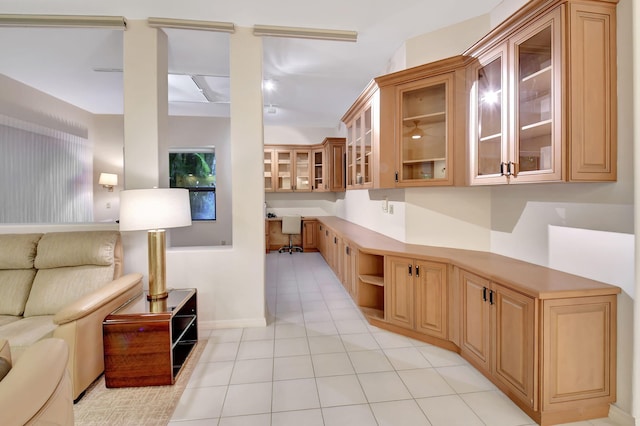 kitchen with built in study area, glass insert cabinets, open floor plan, light countertops, and light tile patterned flooring