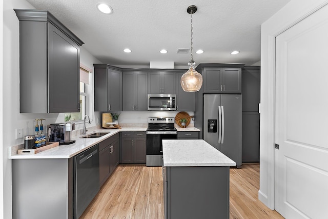 kitchen featuring light wood-type flooring, gray cabinetry, a sink, a kitchen island, and stainless steel appliances